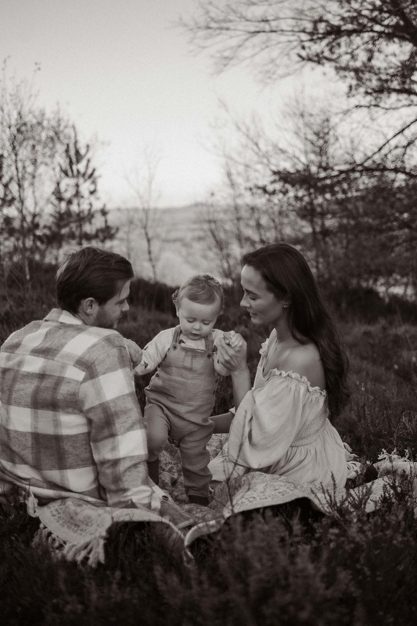 A tender black and white outdoor family portrait taking place in a rustic field setting at twilight.