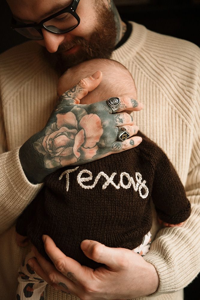 Manchester newborn photographer. Close-up photo showing hands embroidering the word 'Texas' on a dark knit fabric with cream-colored thread.