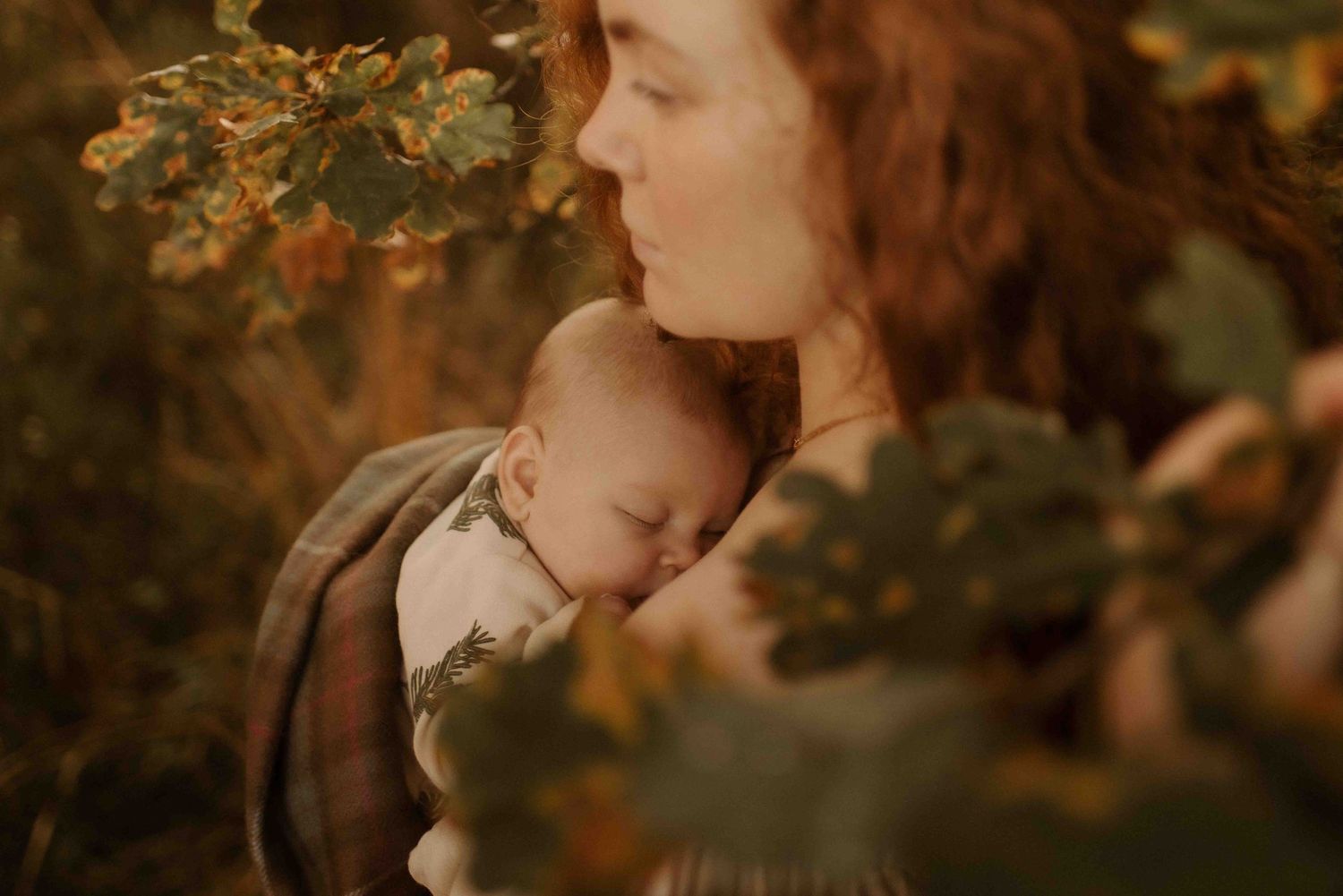 A tender moment captured between parent and sleeping baby amidst autumn foliage in warm earthy tones.