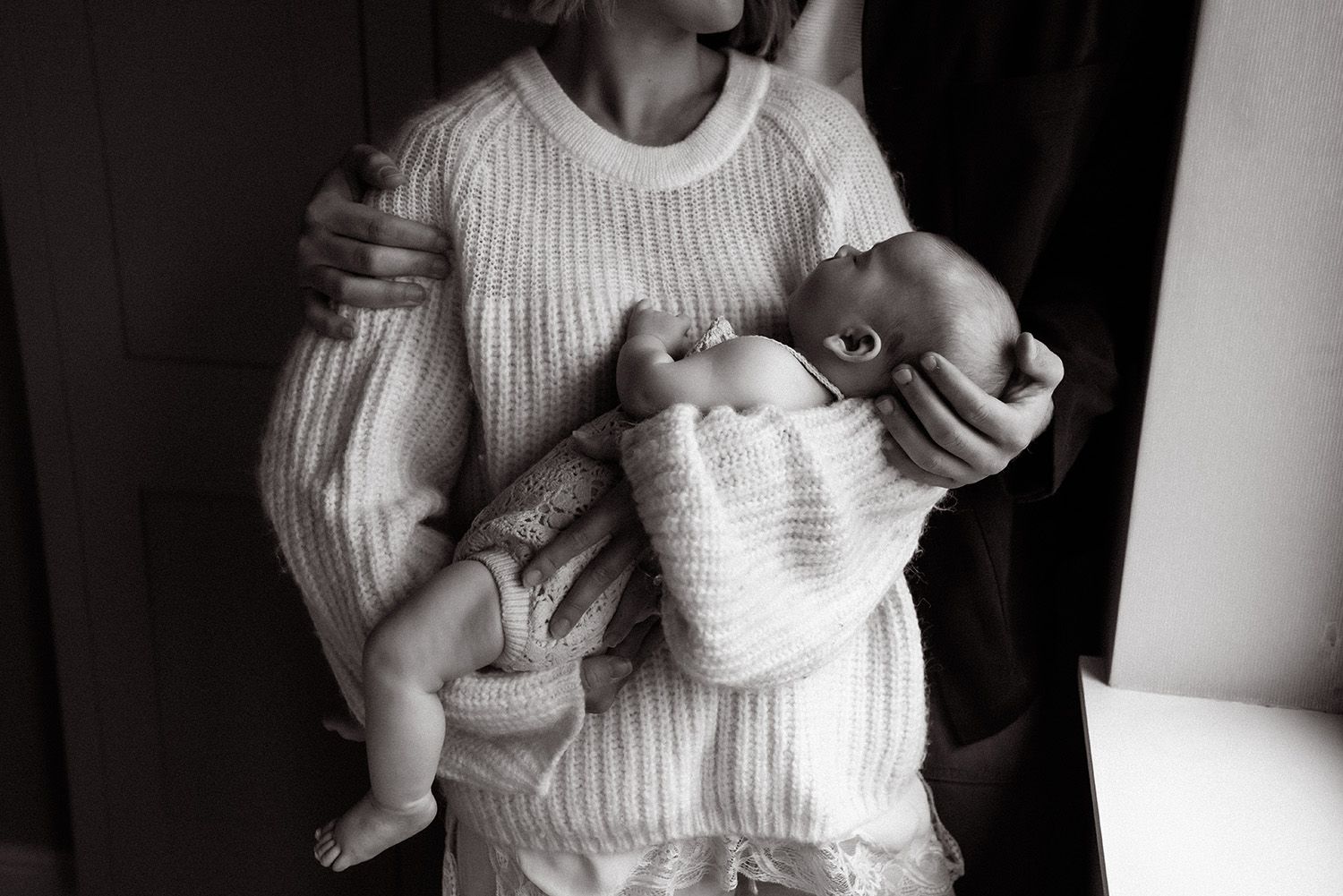 Manchester newborn photographer captures black and white photographs showing someone holding and feeding a baby in a white knit sweater.