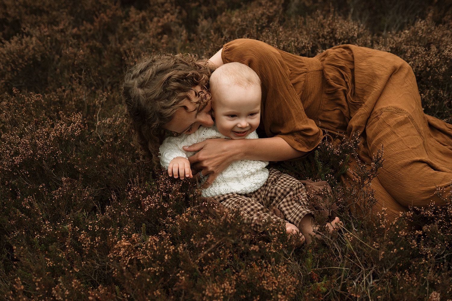 Lancashire motherhood photoshoot. Autumn-themed outdoor photos showing a brown-clad figure resting among fallen leaves and foliage.