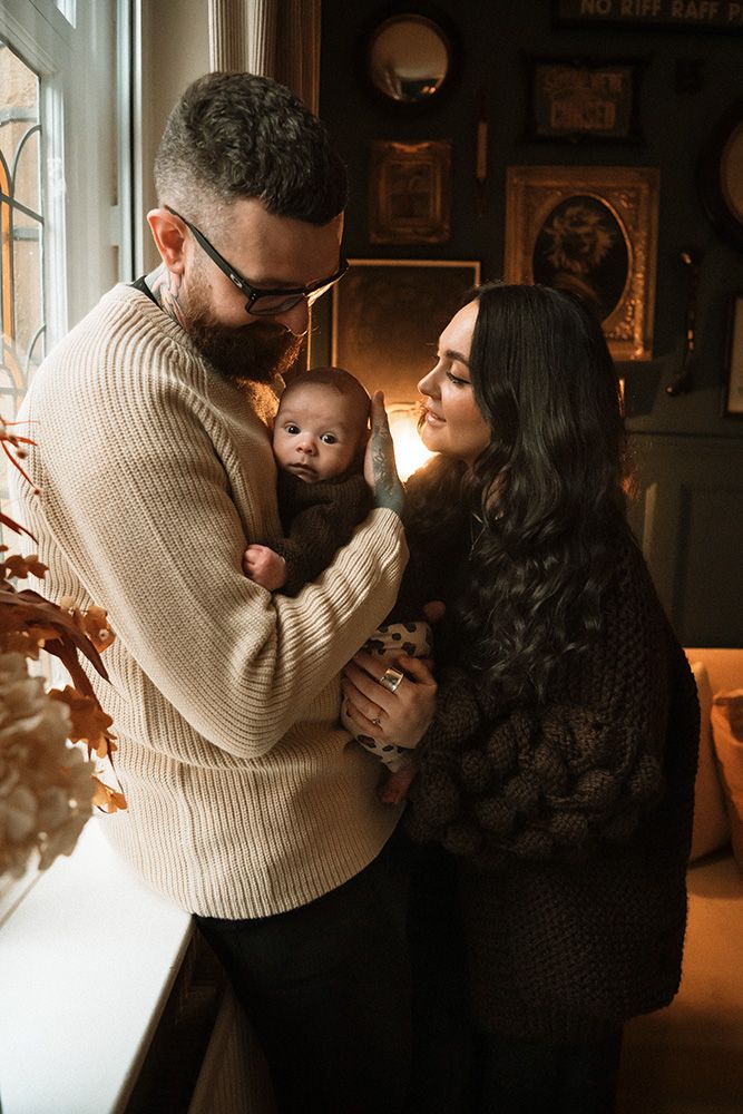 A loving family moment captured in warm lighting as parents embrace their baby in a cozy indoor setting. Newborn photography in Manchester.