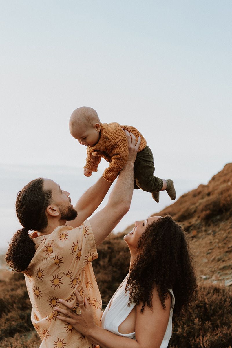 Parents lift and play with their child against a sunset backdrop on a Lancashire hillside during a joyful outdoor family photoshoot