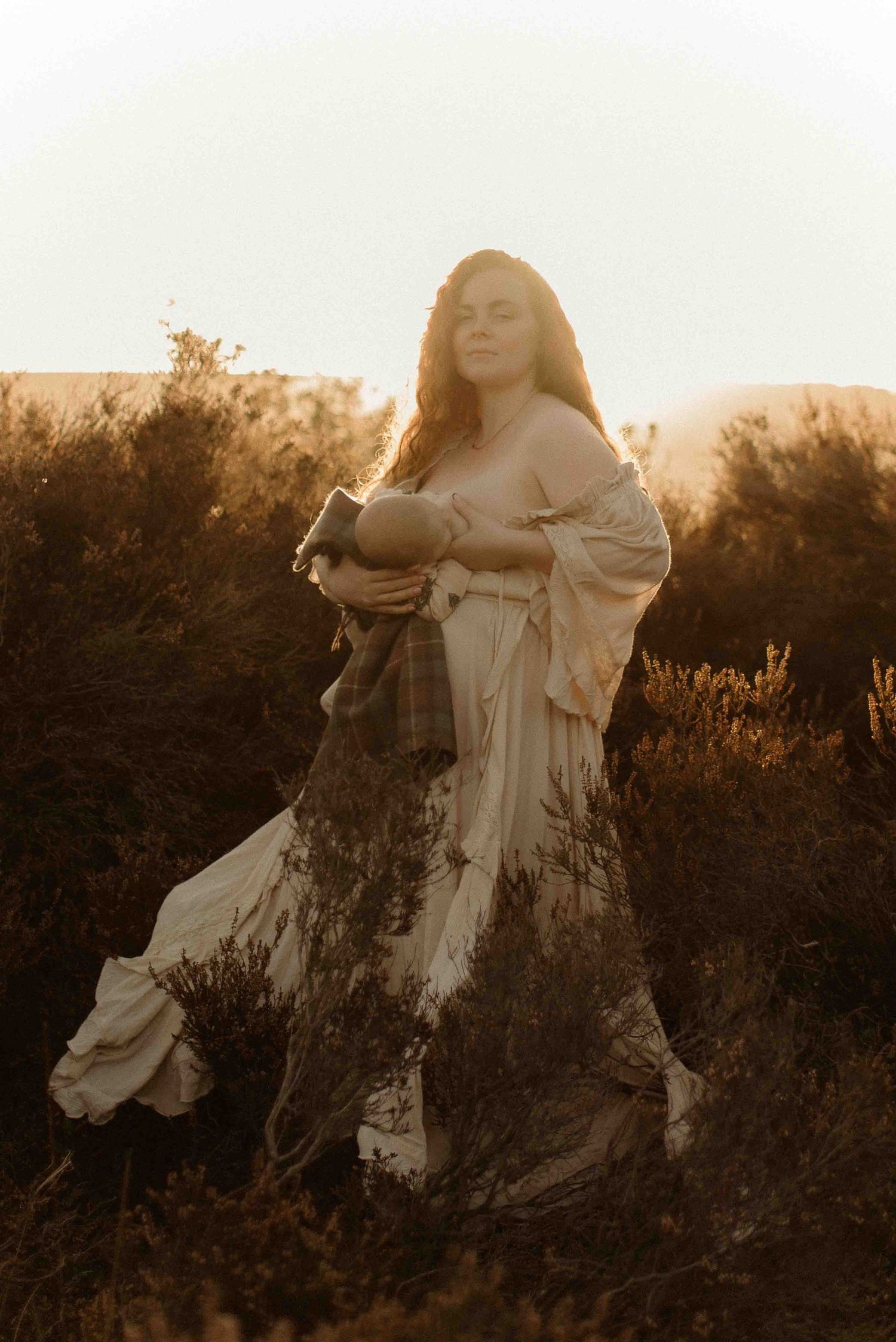 A woman in a flowing white dress poses ethereally in a field at golden hour with sunlit backlighting.