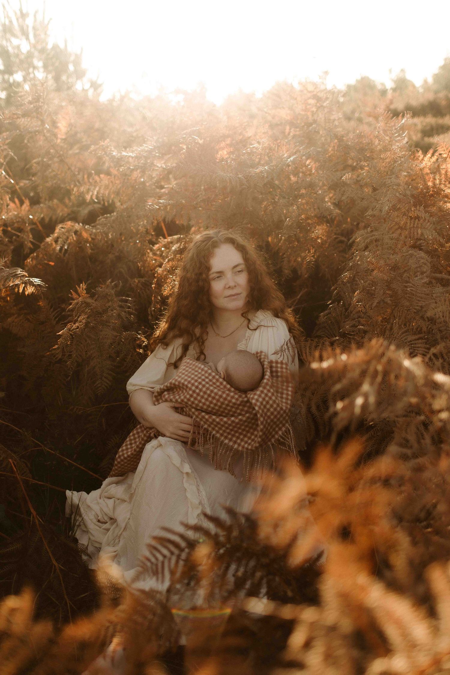 Dreamy golden-hour portrait in a field with tall dried plants and a warm, hazy sunset glow.
