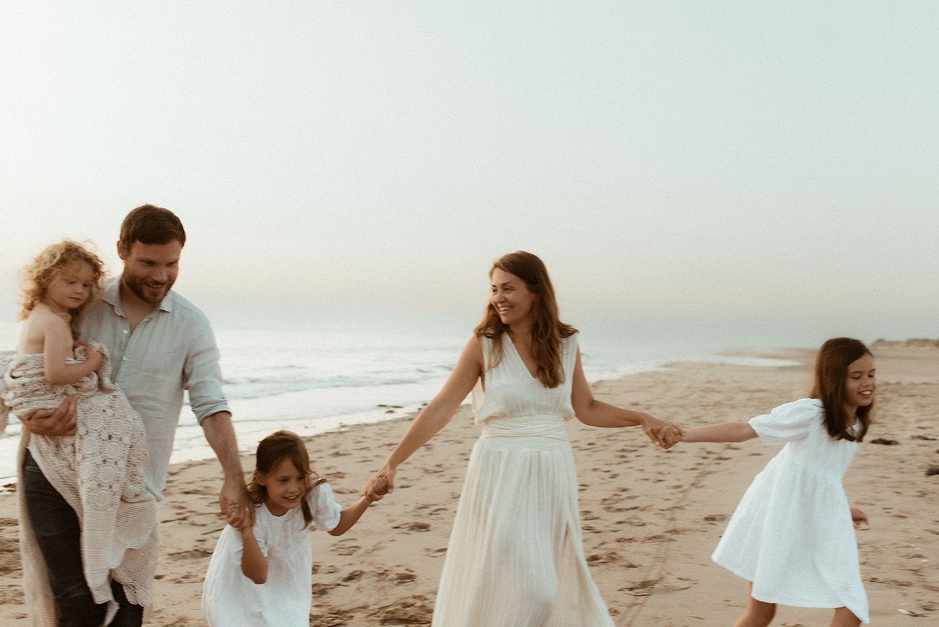 Family of 5 walk together hand in hand at sunset at Formby beach during family photoshoot.
