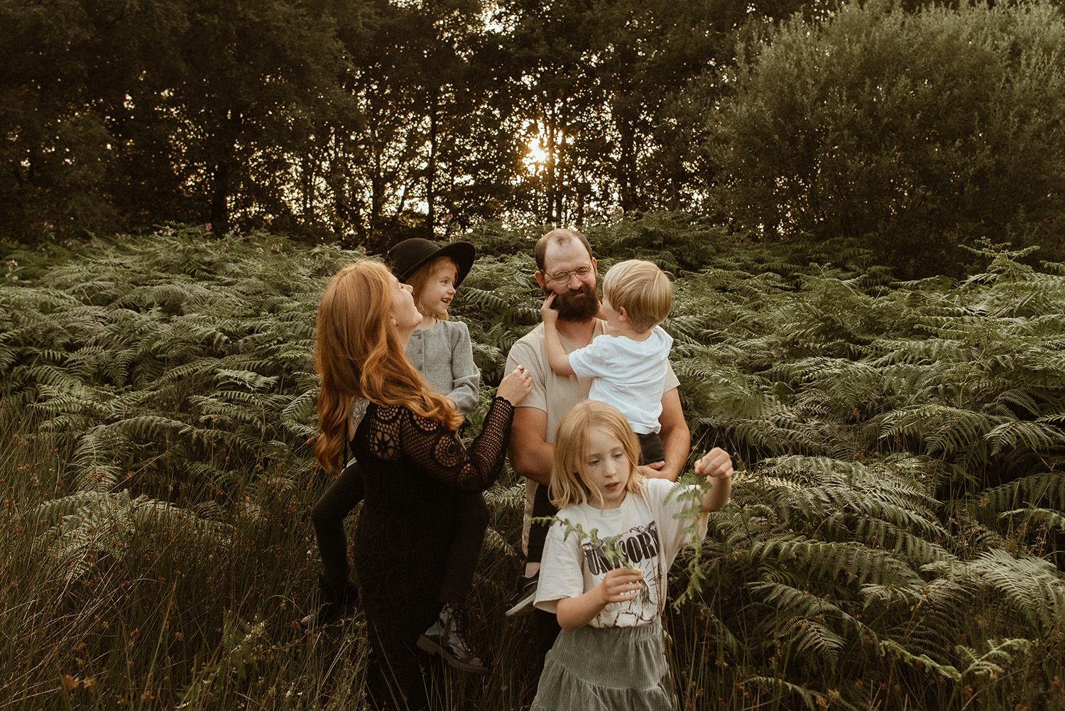 A warm sunset scene among tall ferns as people gather together in an outdoor natural setting during golden hour family photoshoot in Chorley