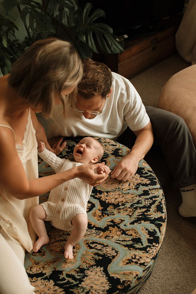 A parent and baby play together with puzzle pieces on a patterned rug in a dimly lit room, during their Manchester newborn photoshoot.