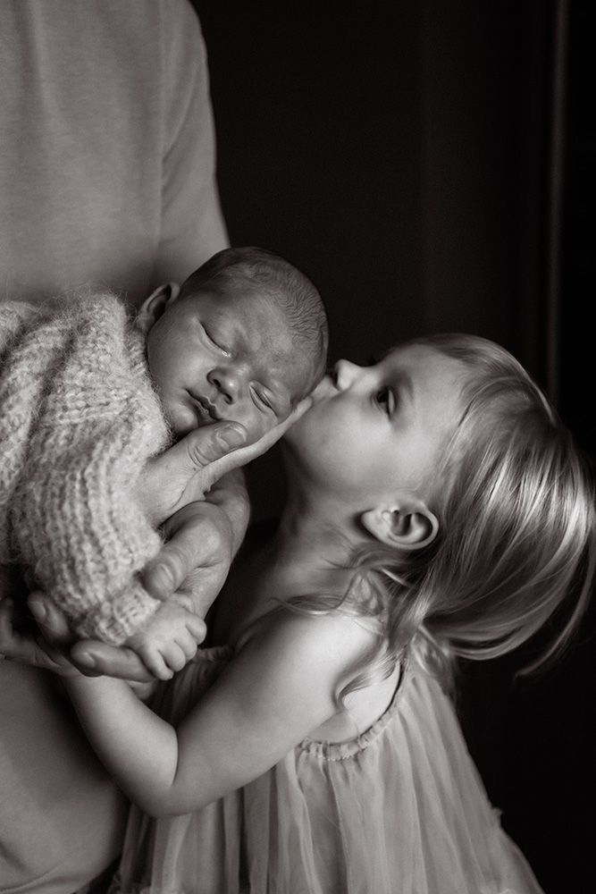 Manchester newborn photographer captures a black & white artistic photo showing a sleeping baby in a white dress against a dark background.