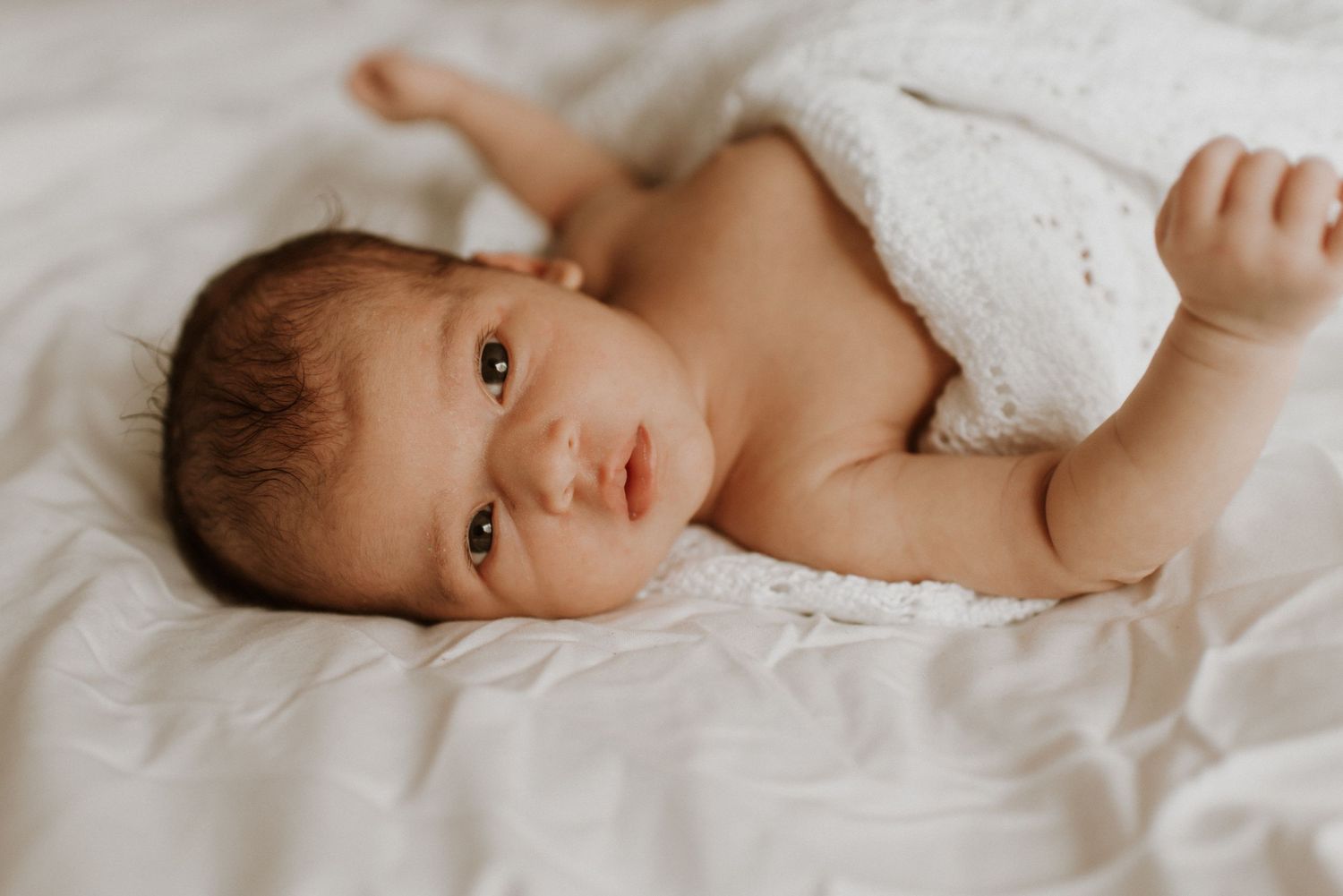 Sweet newborn baby lying on soft white blankets with gentle natural lighting during professional portrait session.