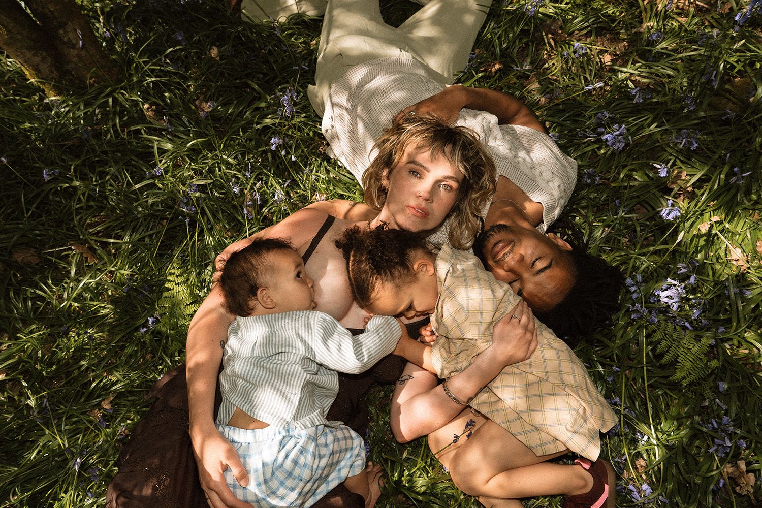 A woman and three children lying together on green grass, viewed from above in a peaceful outdoor setting.