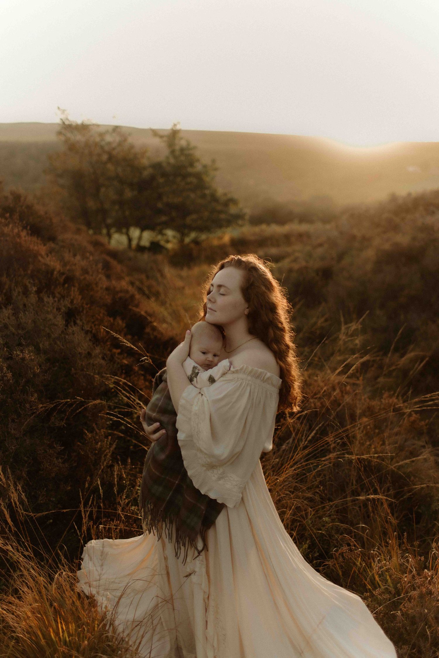 A person in a flowing white dress poses ethereally in a golden meadow at sunset with rolling hills in the background.