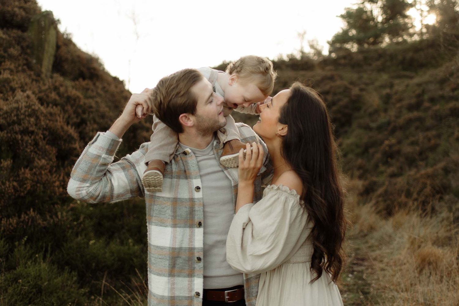 Family shares tender moment together outdoors during golden hour on hillside in warm autumn light.