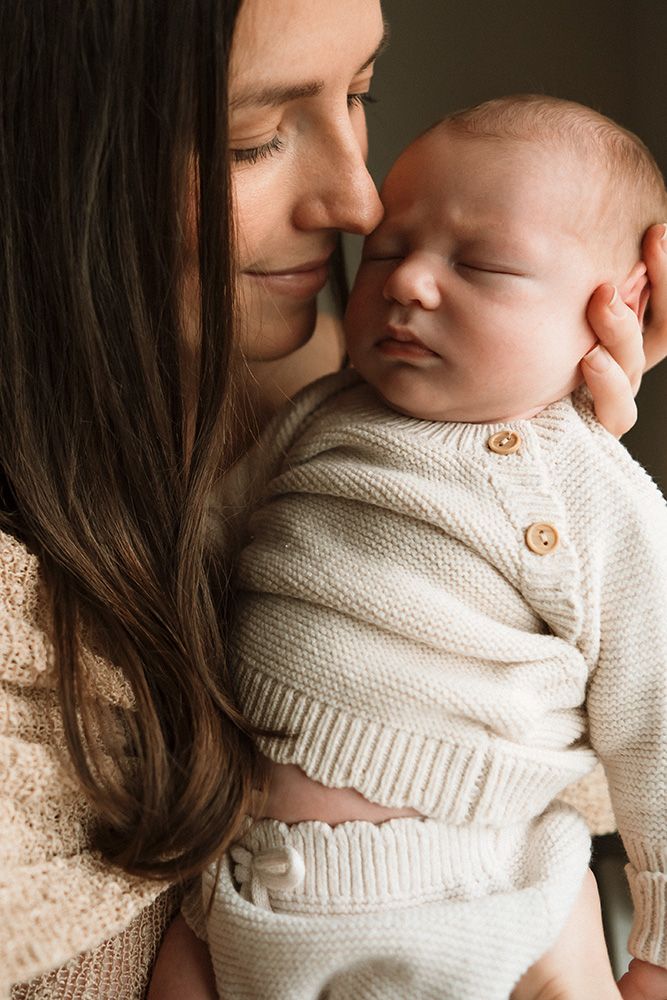Newborn photoshoot Manchester. A tender moment captured between Mum and sleeping newborn baby in matching cream-colored knit sweaters.