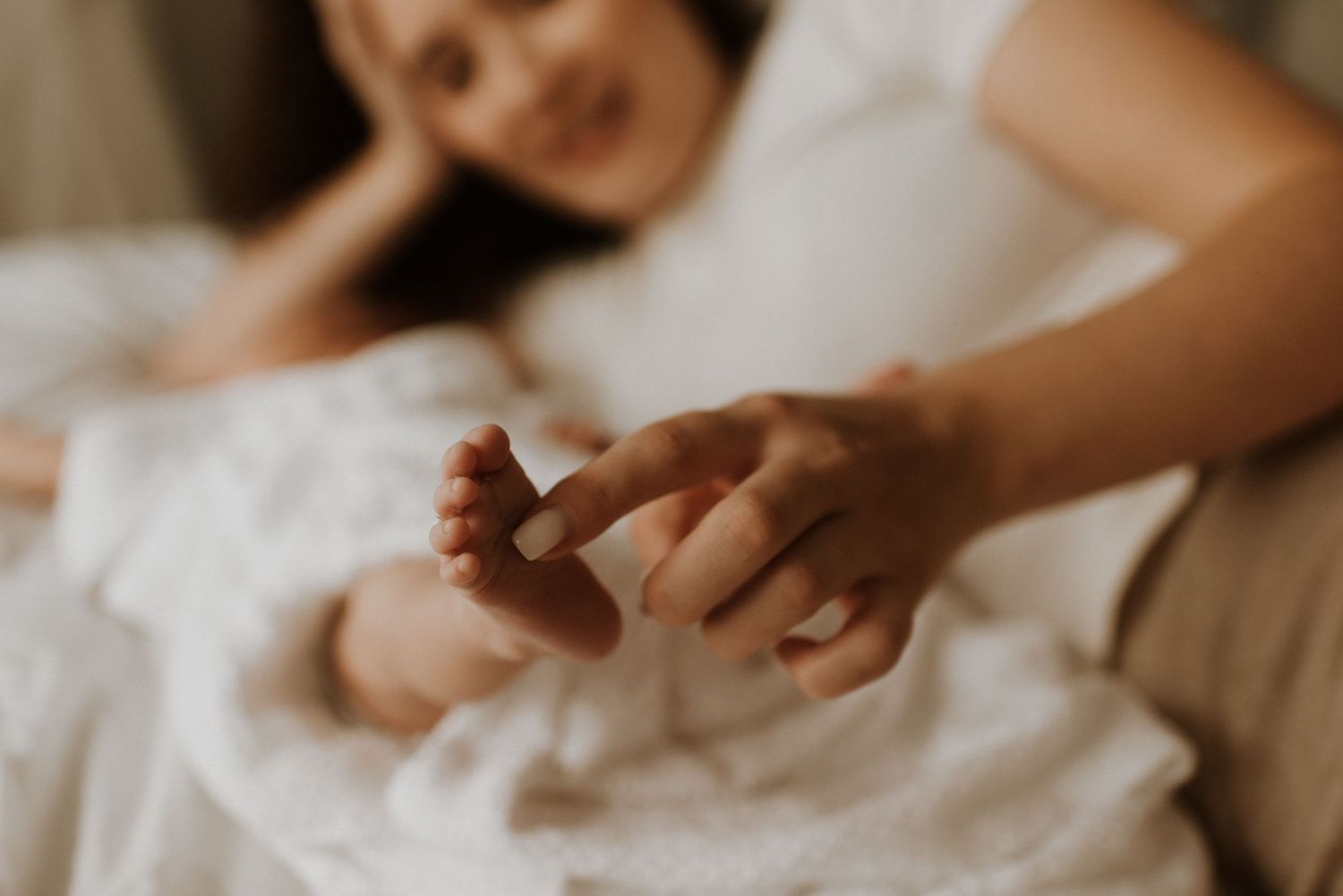 A close-up view of tiny baby feet being gently touched against white bedding in warm lighting.