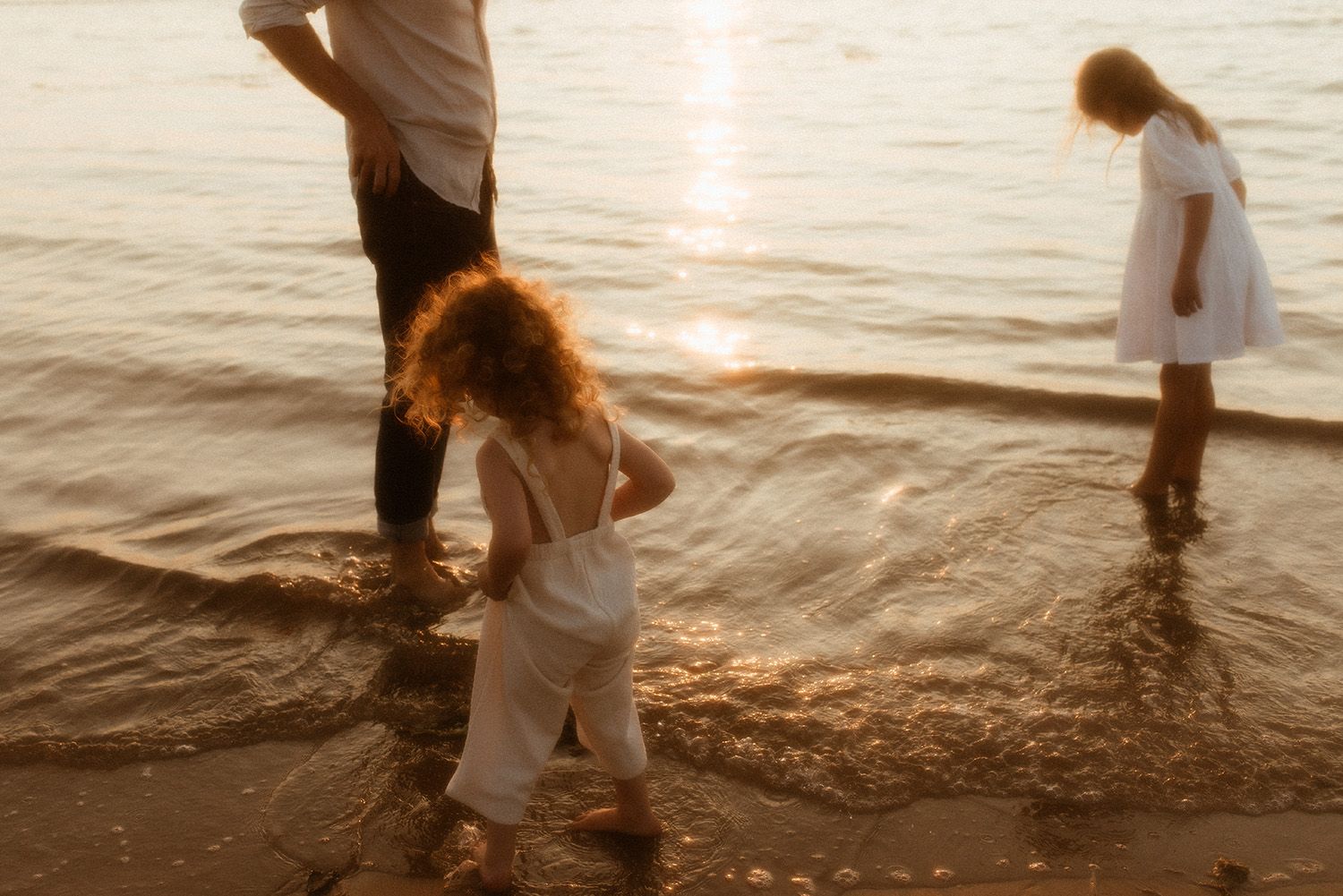Family playing in shallow ocean waves at sunset with light reflecting off the tranquil water during family photography session in Lancashire