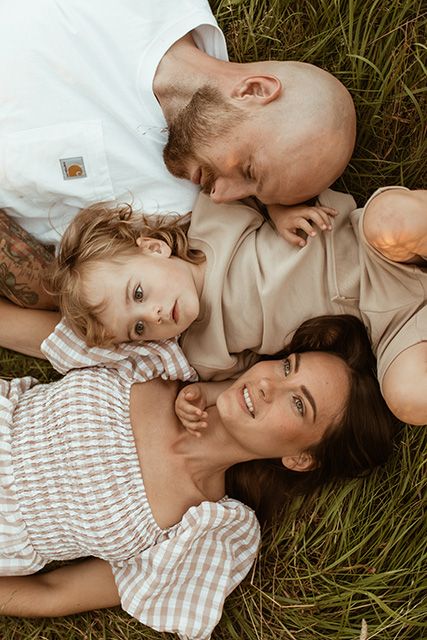 A family lying together in the grass at sunset, wearing earthy coloured clothing during relaxed family photoshoot in Lancashire