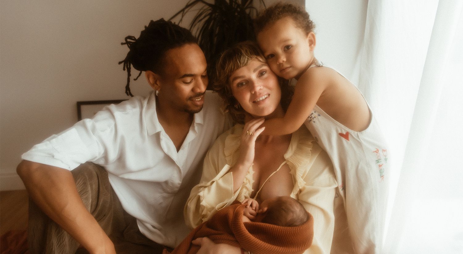 A cosy family moment captured in warm lighting as they cuddle together near a window during in home newborn photoshoot lancashire