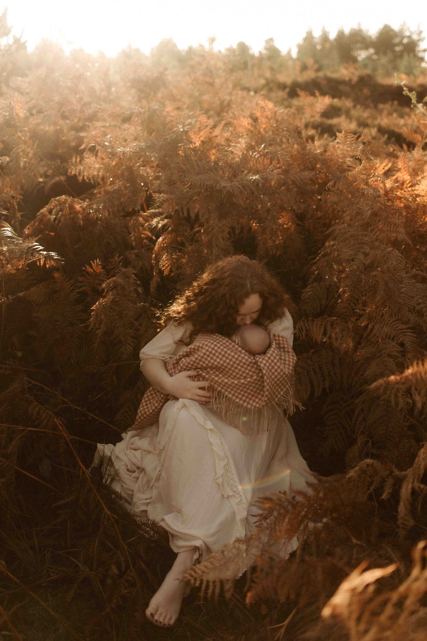 A dreamy golden-hour scene shows someone in a white dress sitting among tall autumn ferns in nature.
