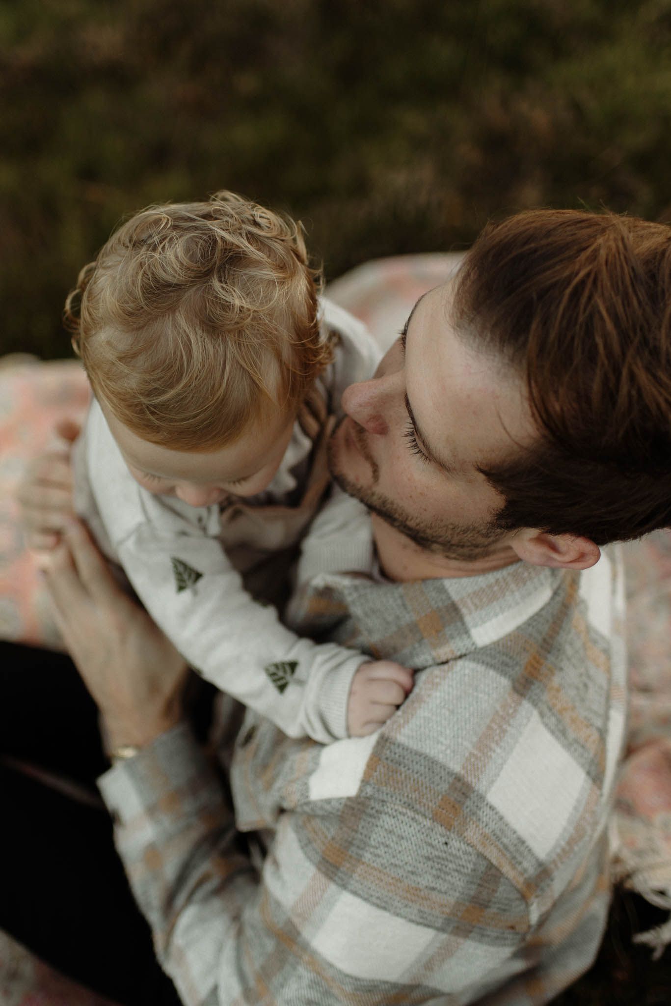 A tender moment captured between adult and young child outdoors wearing plaid and casual clothing.