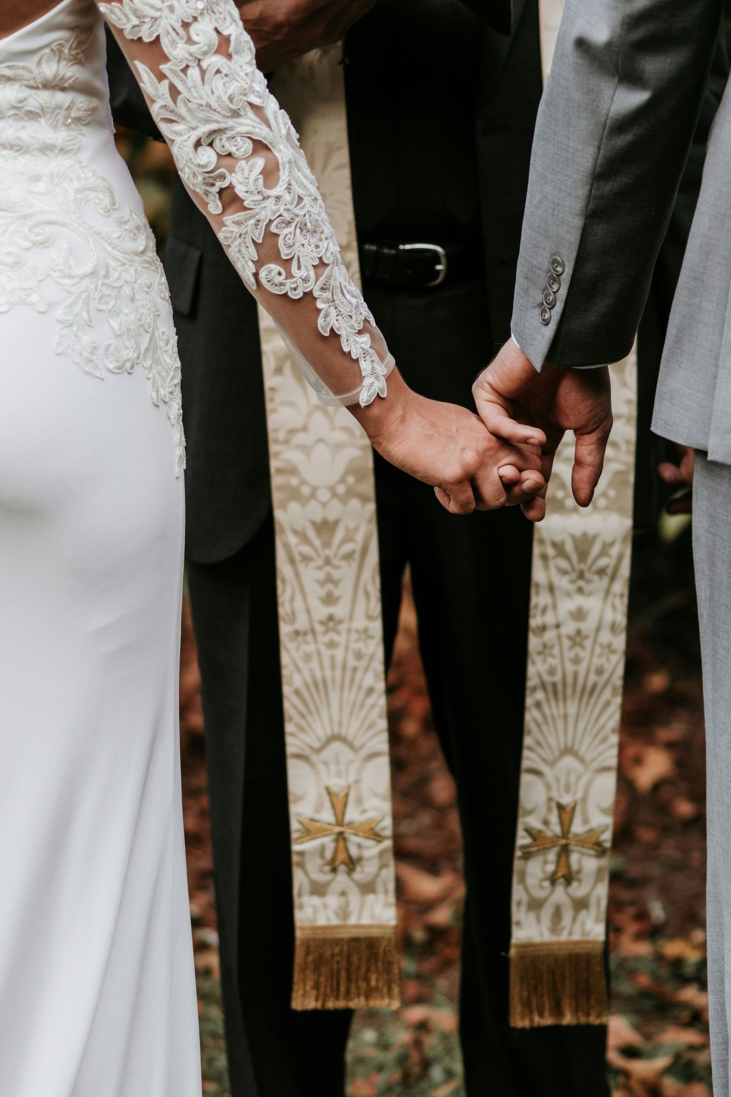 Close-up of a couple holding hands at their wedding ceremony with ornate clergy stoles visible in the background.