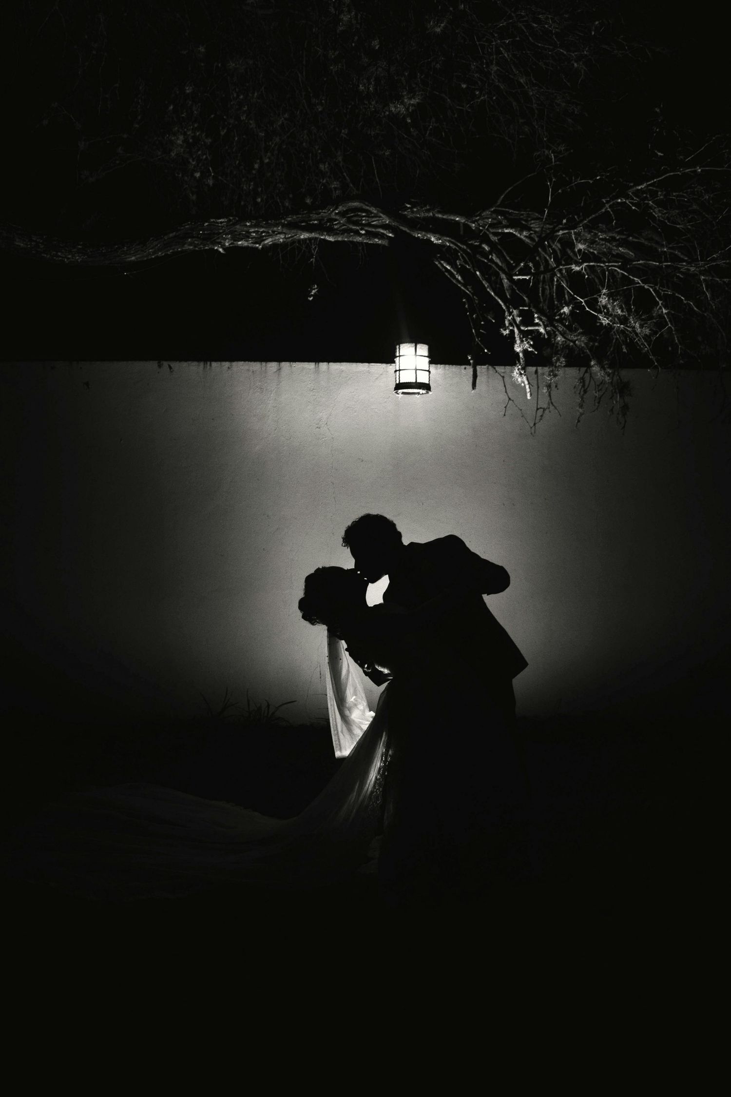 A dramatic black and white silhouette of two figures dancing in darkness with a single light illuminating from above.
