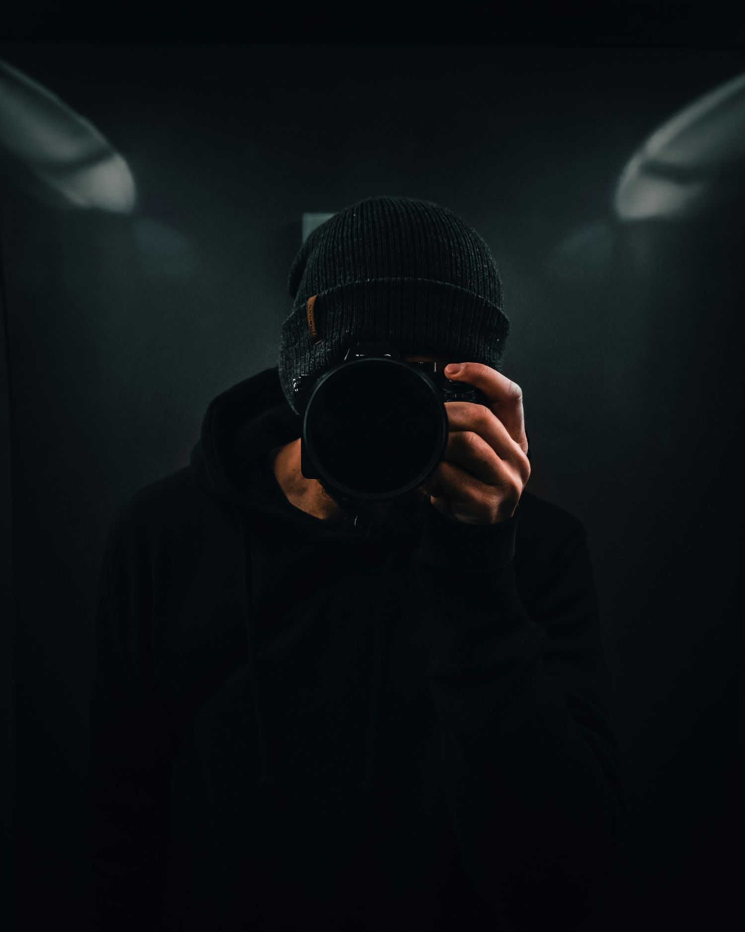 Dark silhouette of a photographer wearing a beanie holding a camera in a dramatic low-key lighting setup.