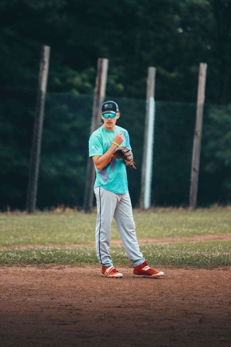 Baseball player stands on field in teal jersey and gray pants preparing to pitch ball during practice session.