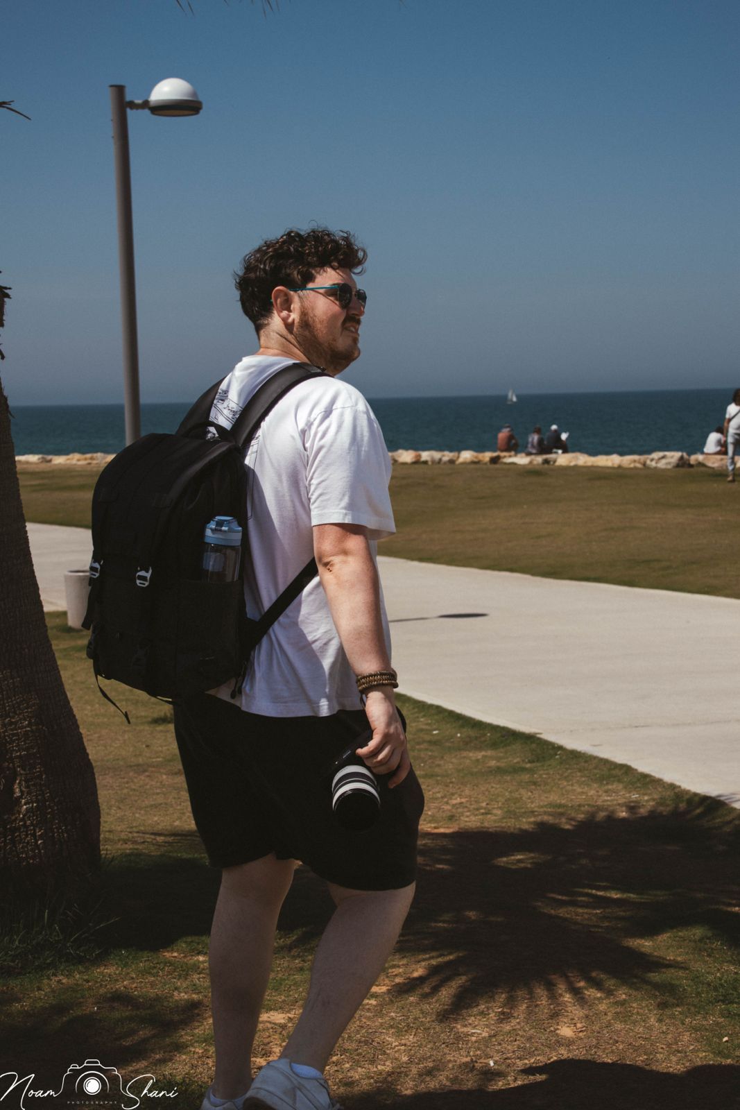 Person with backpack walking along coastal pathway on sunny day with ocean view.