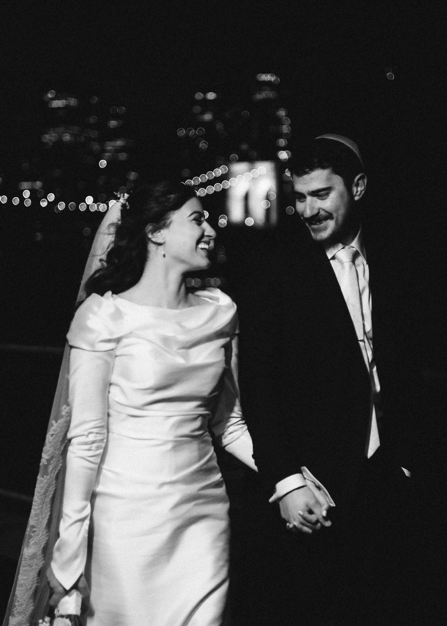 A couple in formal wedding attire shares an intimate moment during their black and white nighttime photo session.