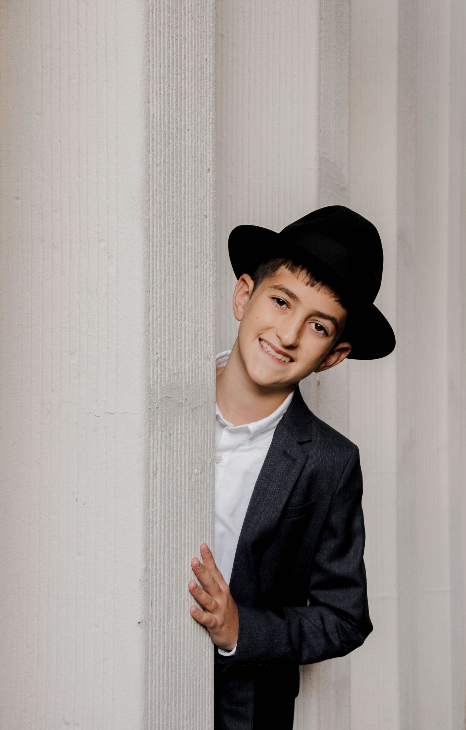A playful sequence showing someone in a black suit and baseball cap posing against a white column background.