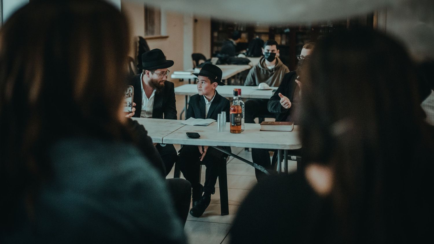 Students working at tables in a dimly lit classroom or study space.