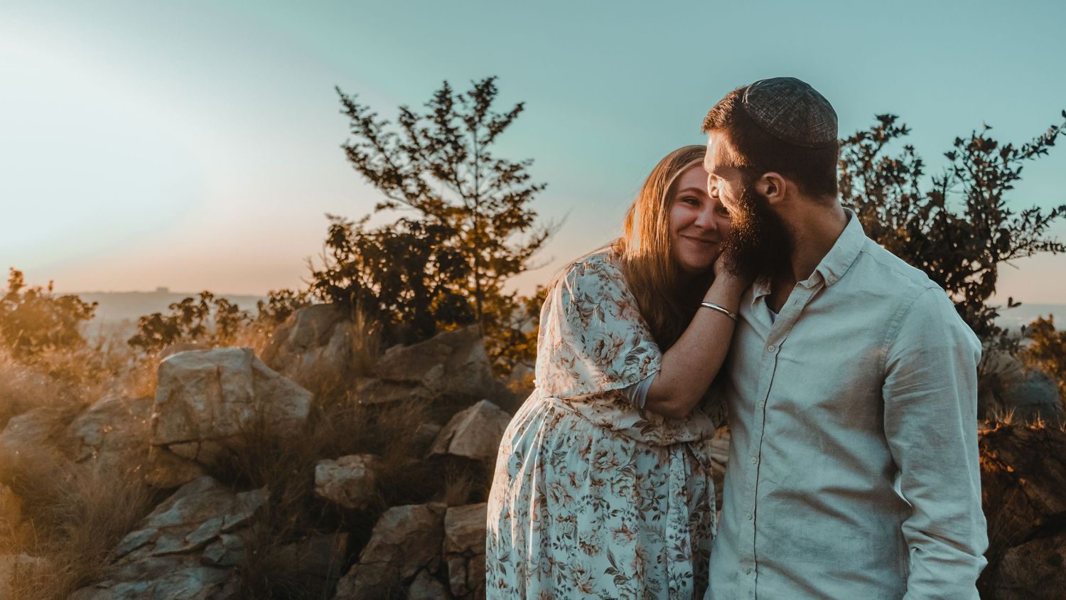 A romantic moment captured in nature during sunset with soft golden lighting and trees in the background.