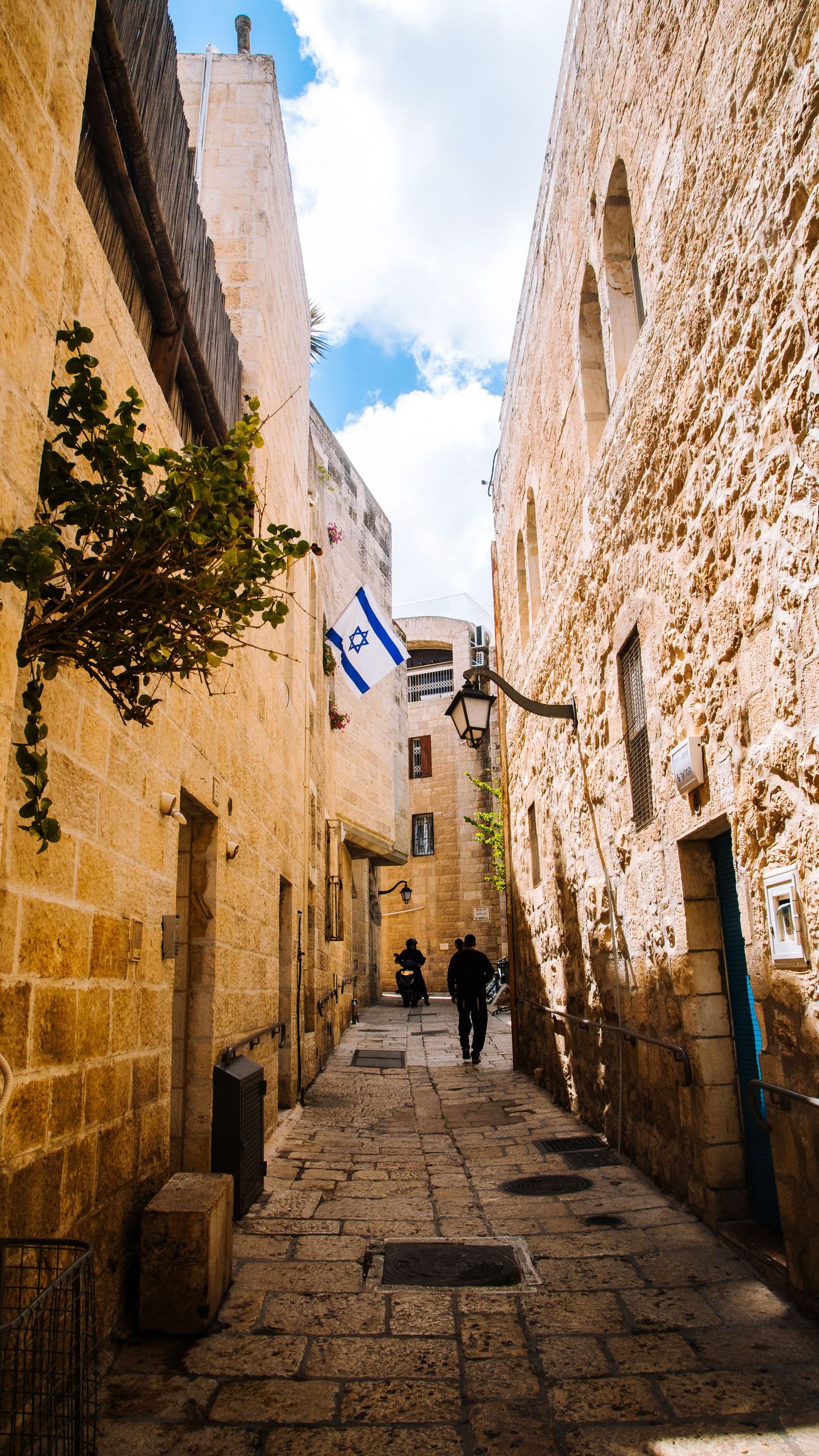 Narrow stone alley in Jerusalem with Israeli flag and ancient architecture.