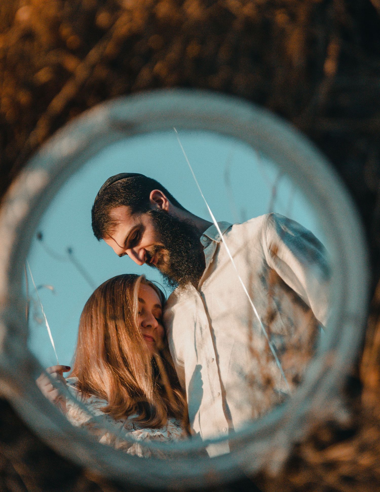 A romantic scene reflected in a round mirror against a blurred dark background with turquoise tones.
