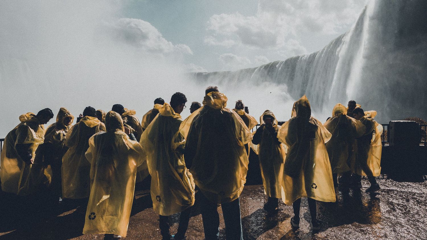 Panoramic view of people silhouettes walking against a cloudy sky with dramatic lighting.