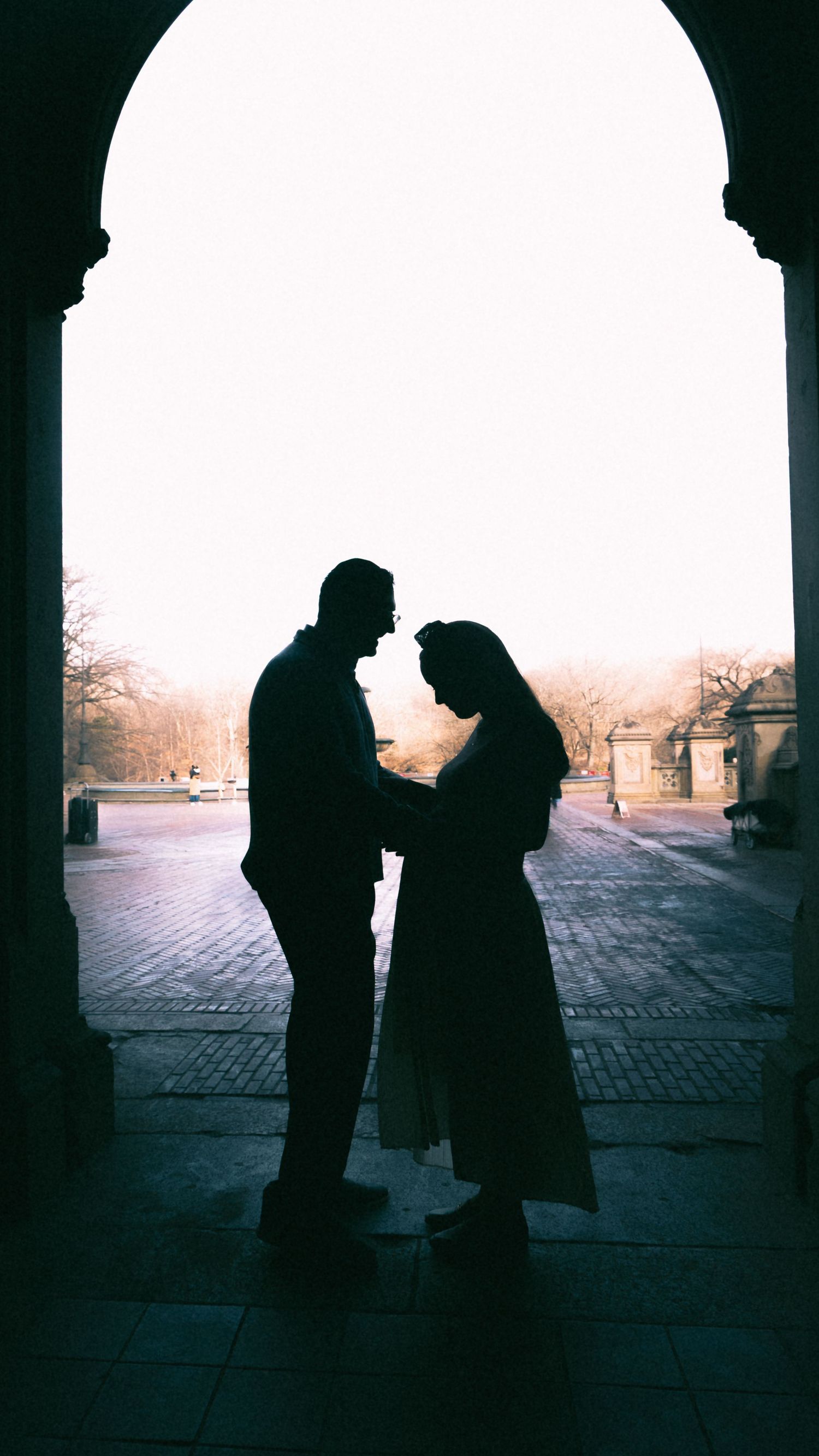 Silhouettes of two people standing in conversation under a dark archway at dusk.