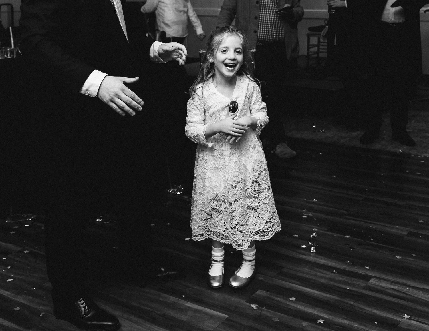 A black and white photo sequence showing a toddler in a lace dress walking across a wooden floor.