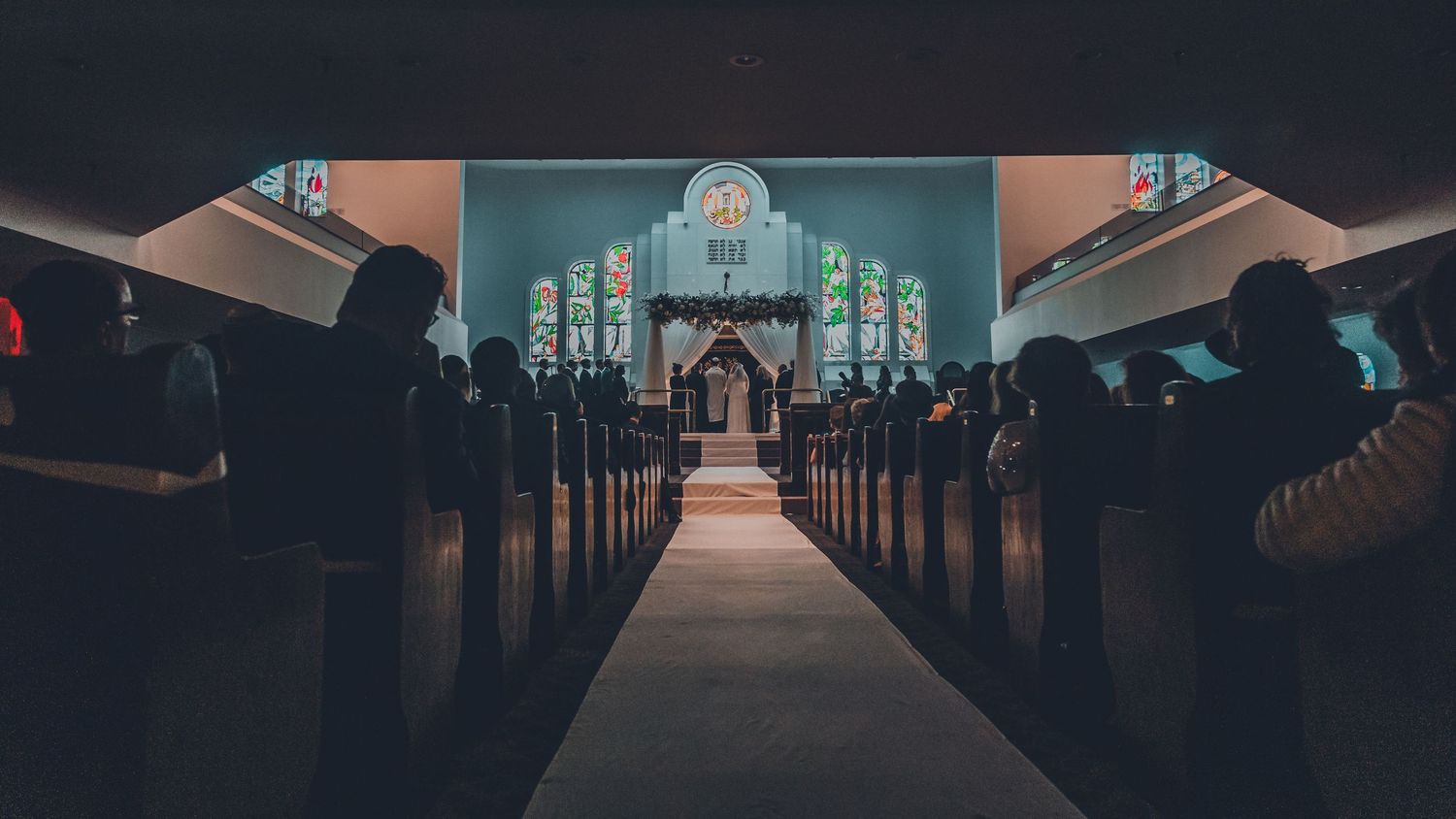 Dark church interior with illuminated stained glass windows and center aisle.