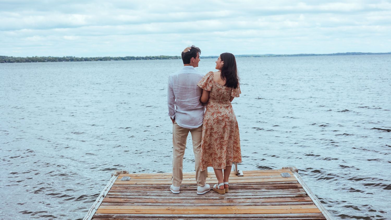 Couple sits together on a wooden dock overlooking a tranquil lake during sunset.
