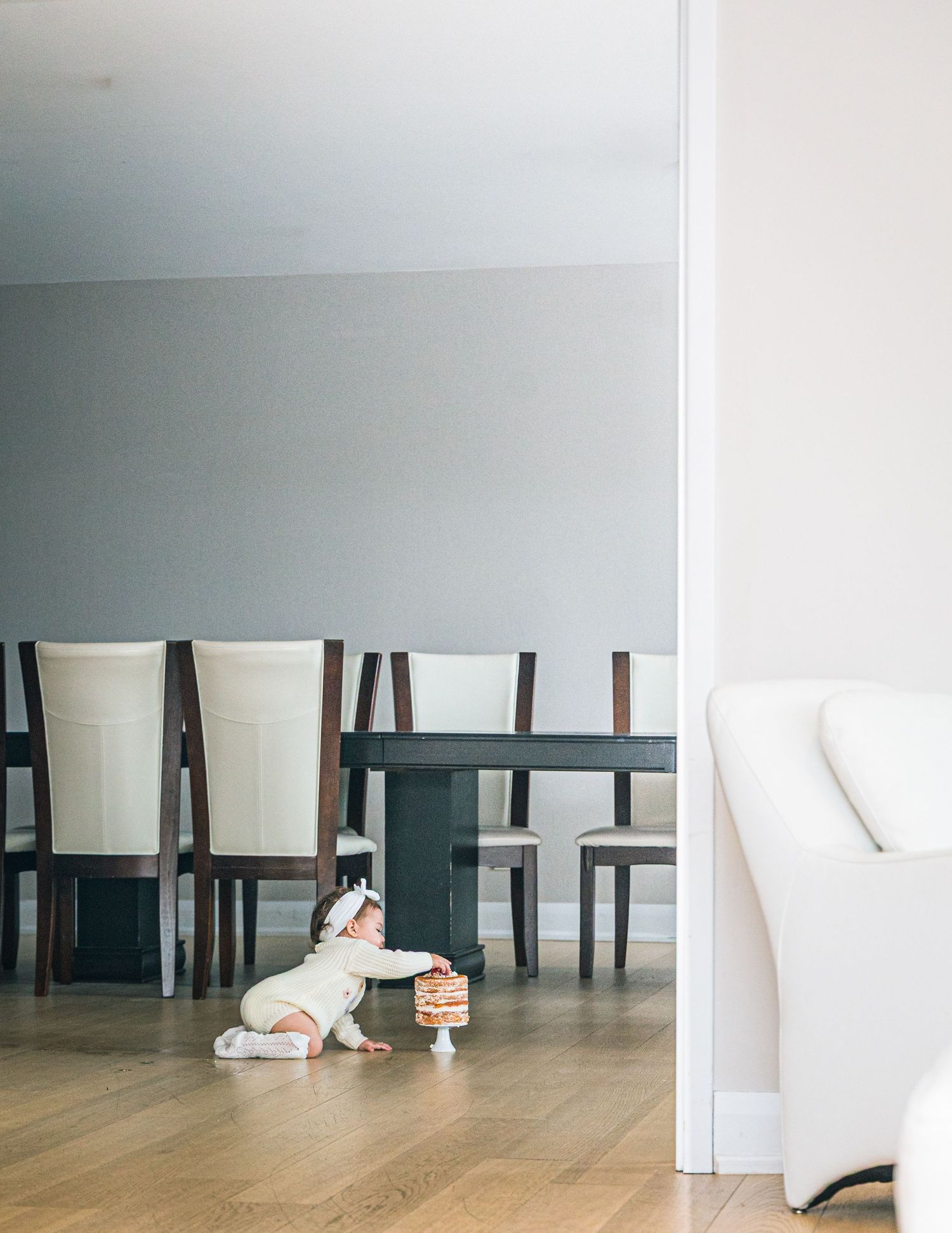 A person lying on the floor in a minimalist room with white walls and dark wooden chairs.