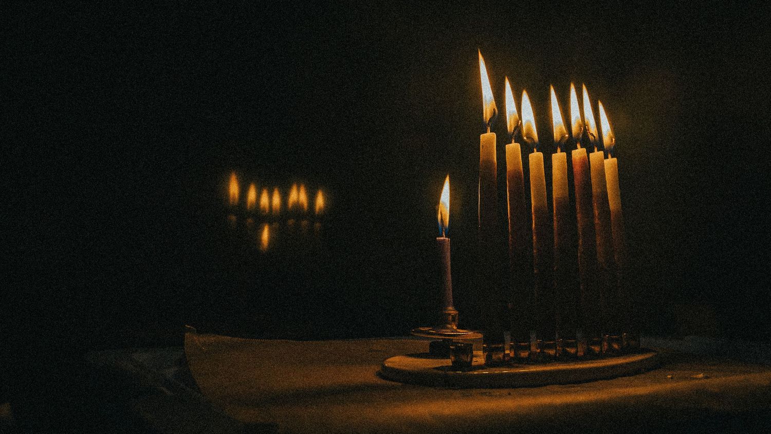Glowing Hanukkah menorah candles illuminated against dark background.