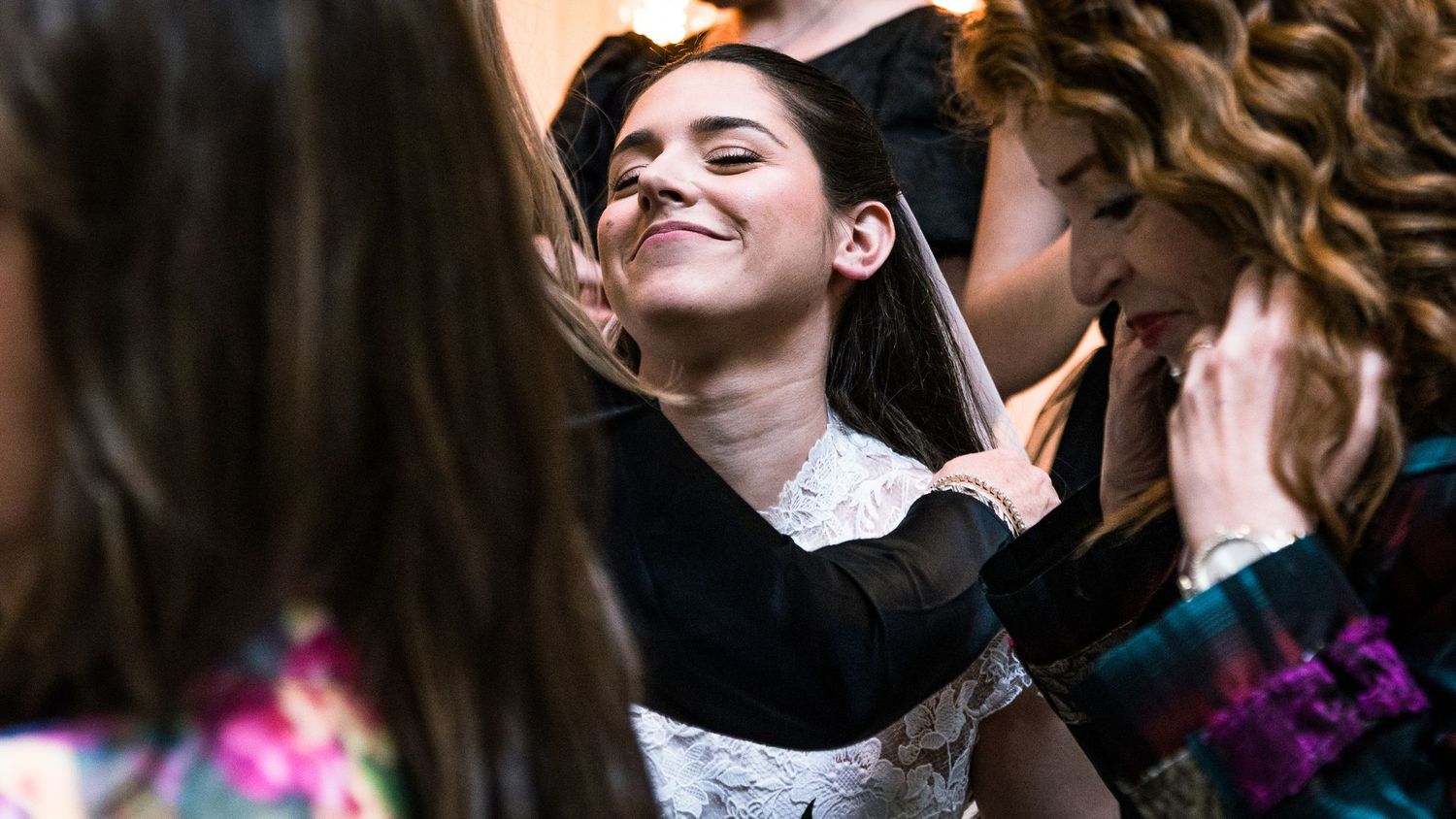 A student in graduation attire smiles while being helped with their cap during a commencement ceremony.