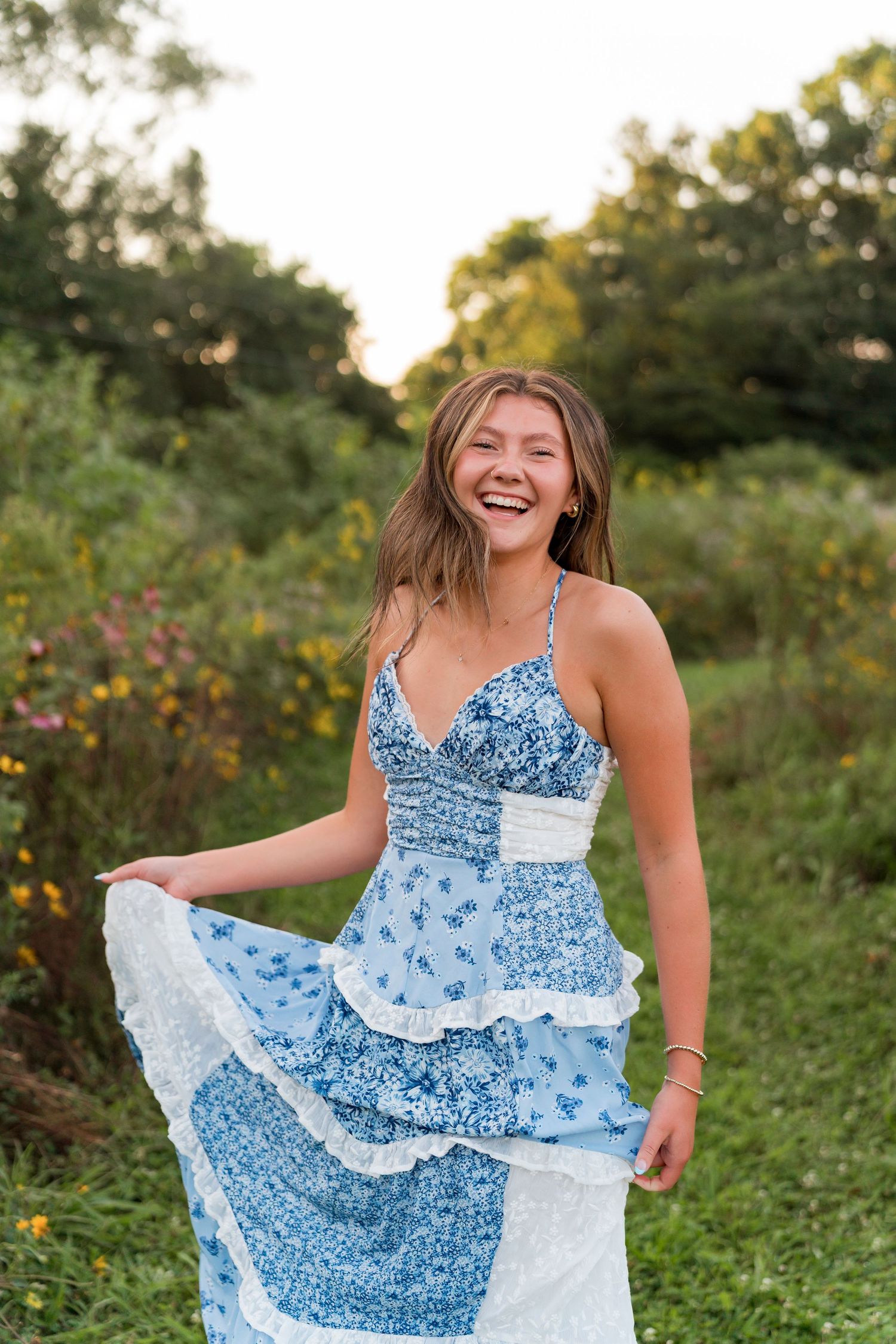 A person in a blue floral dress twirls joyfully in a sunlit meadow with wildflowers during golden hour.