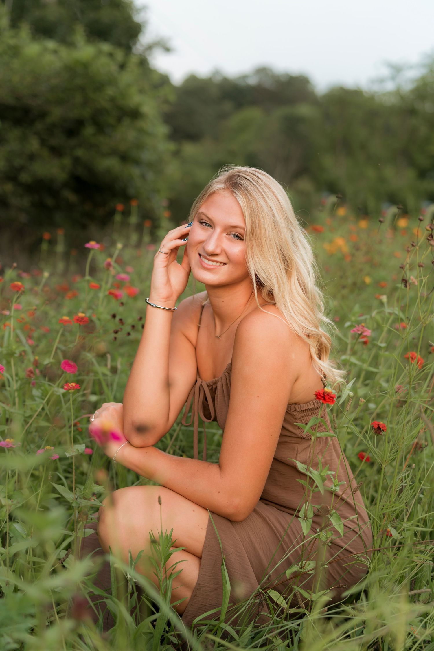 A person poses in a brown dress among vibrant red wildflowers in a lush summer meadow.