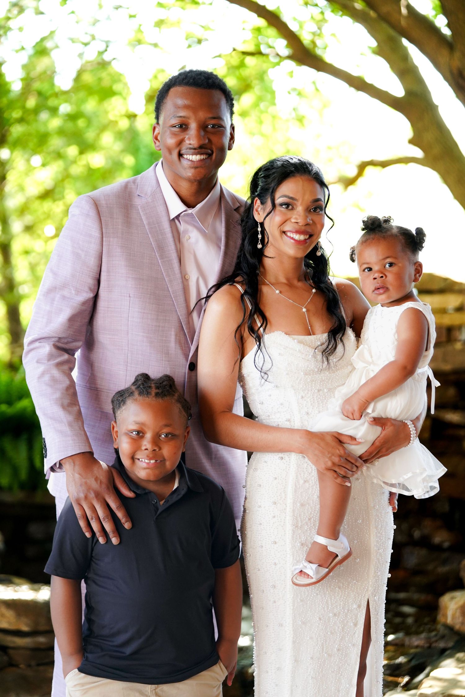 Happy family group poses together outdoors under a shady tree.