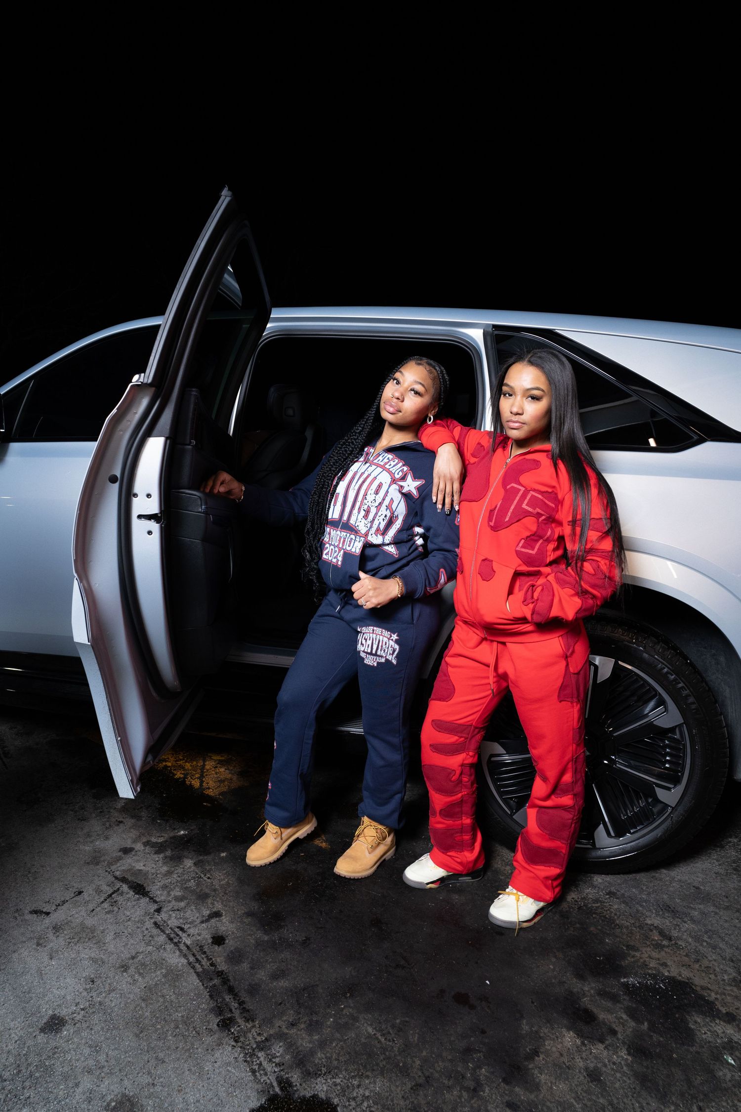 Two small children sit in a car wearing contrasting navy and red outfits with matching footwear.