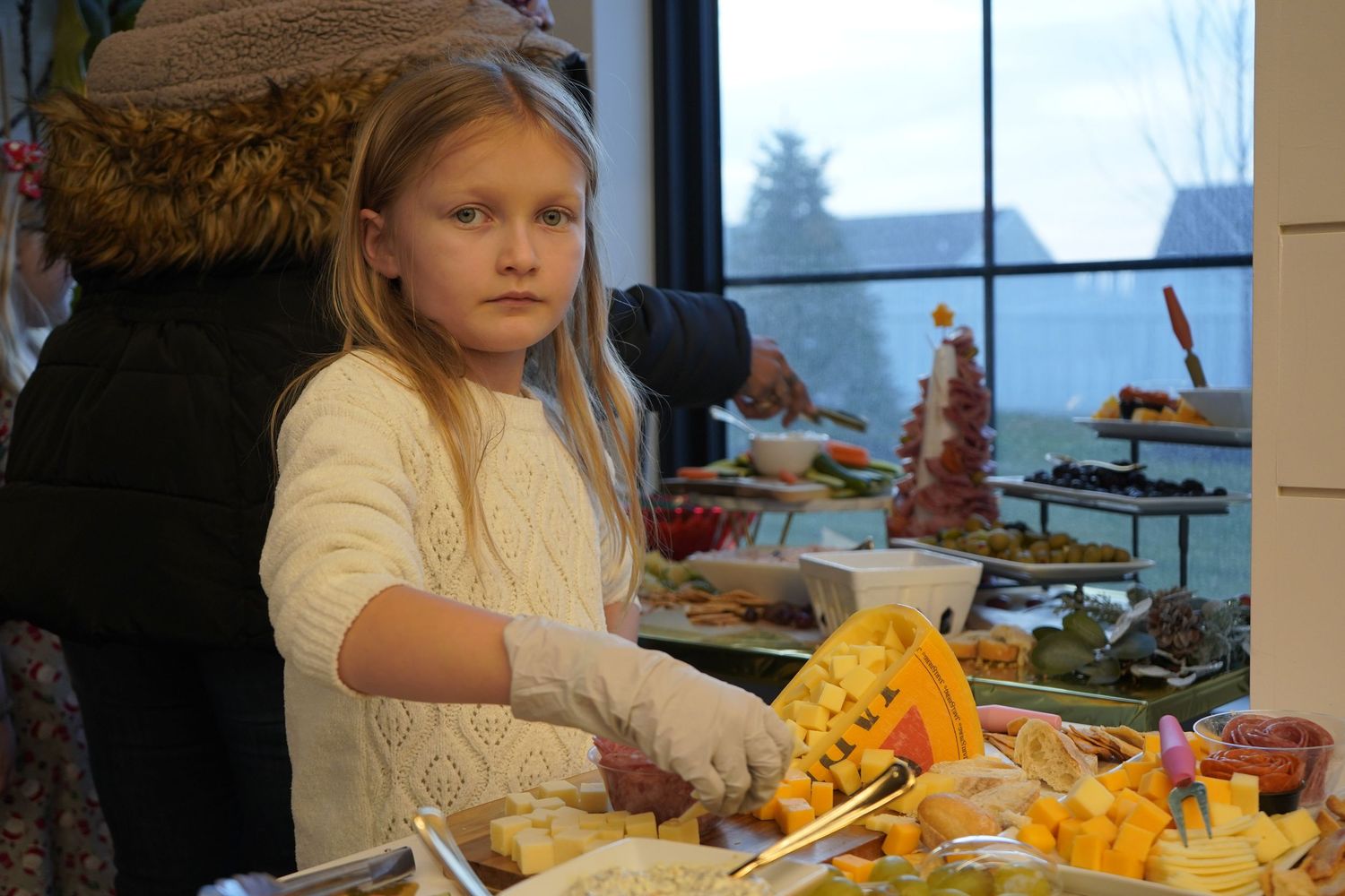 A young guest serves themselves food at a buffet table in a bright dining room with windows.