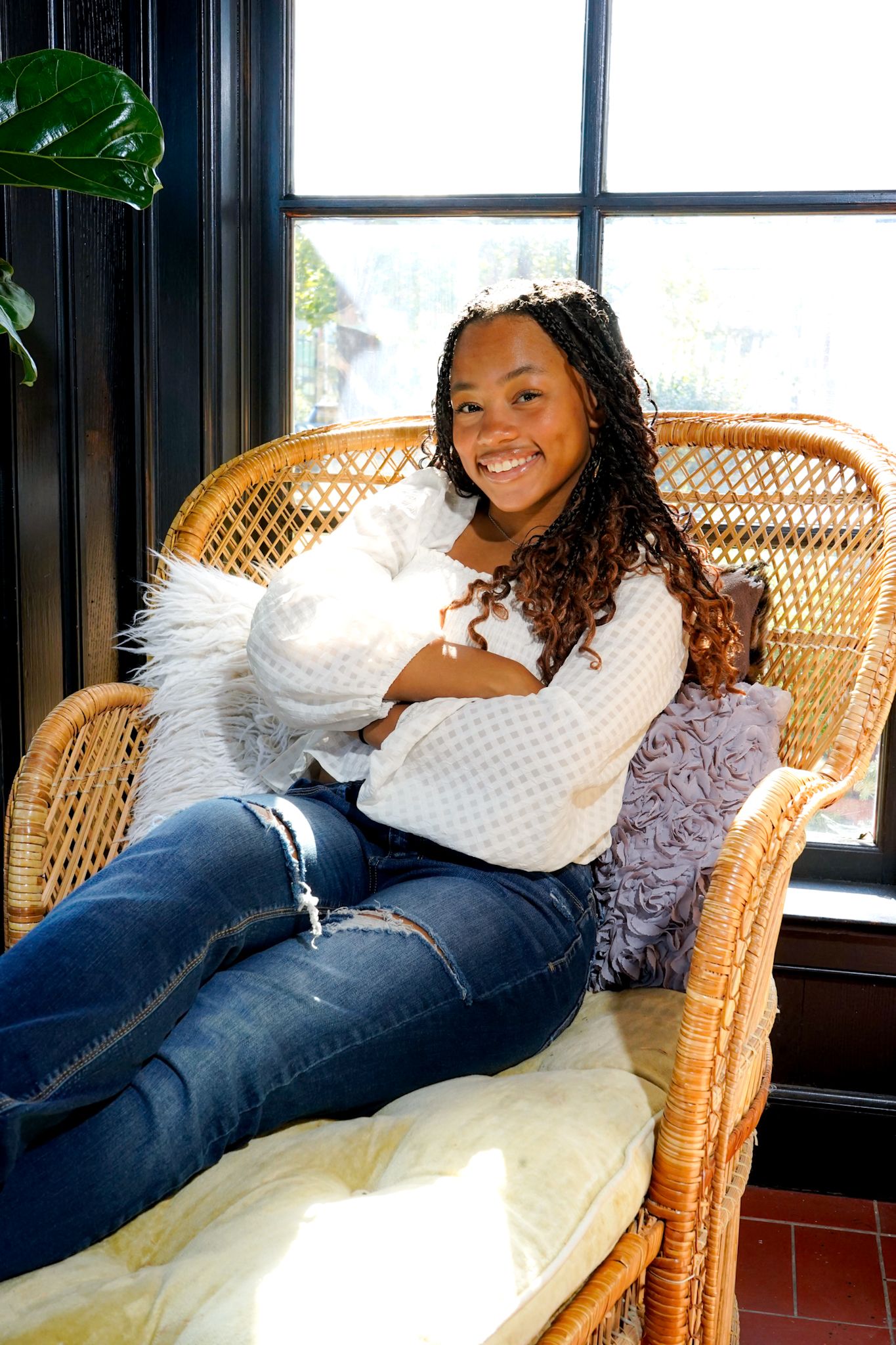 A series of relaxed poses on a wicker chaise lounge chair near a window with natural lighting.