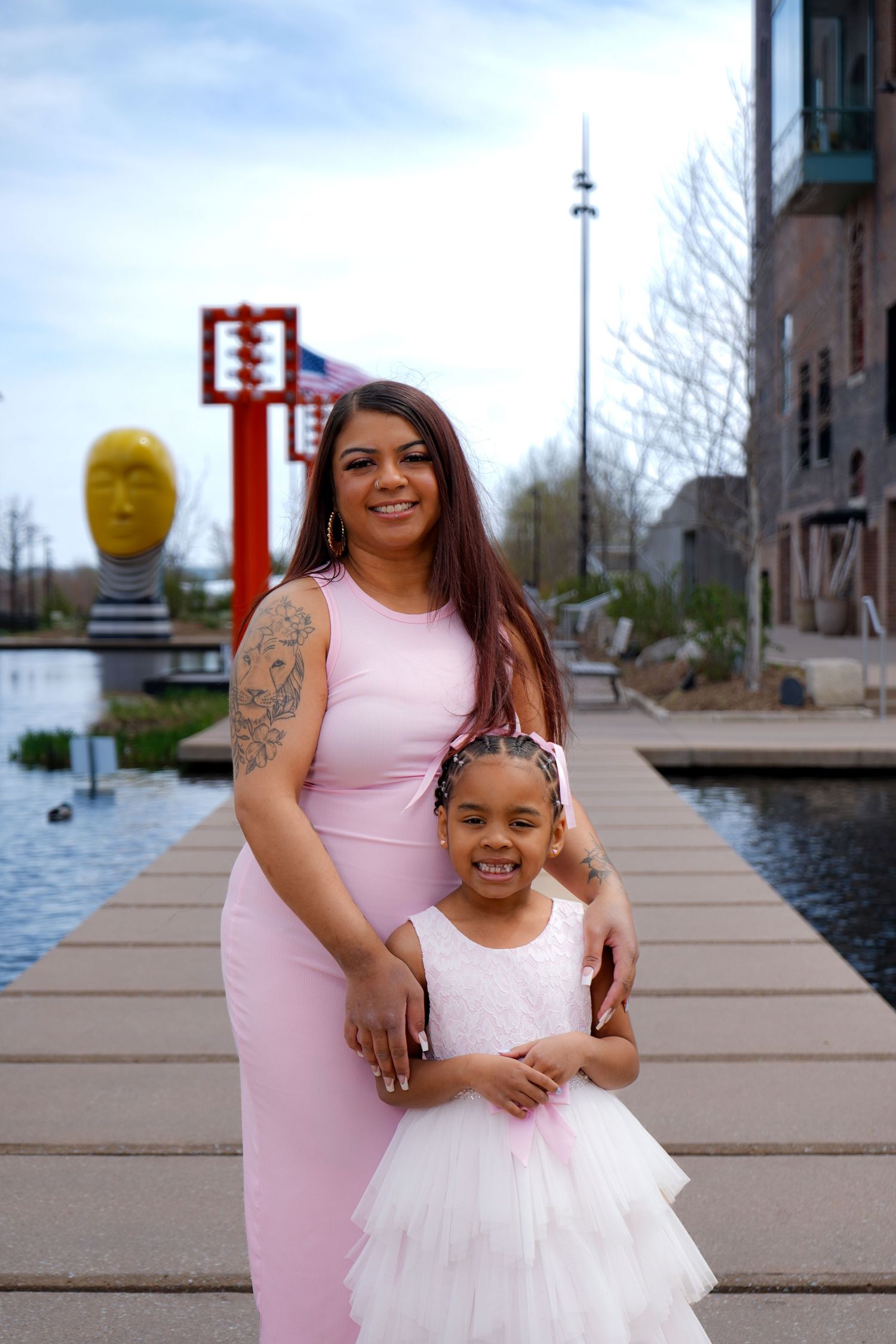 A parent and child in matching pink and white outfits pose together on a wooden dock by the water.